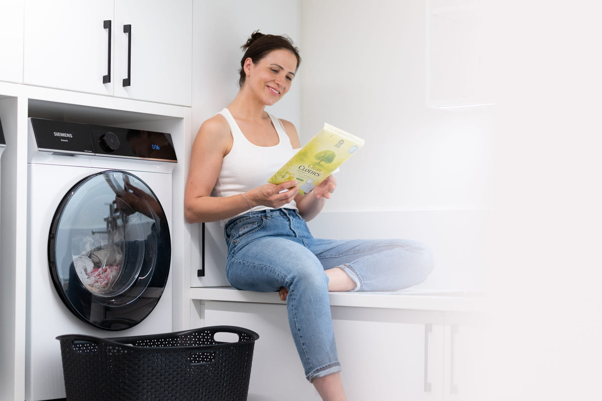 Lena von MamaWillow sitzt in der Waschküche und liest die Clean-Clothes-Packung