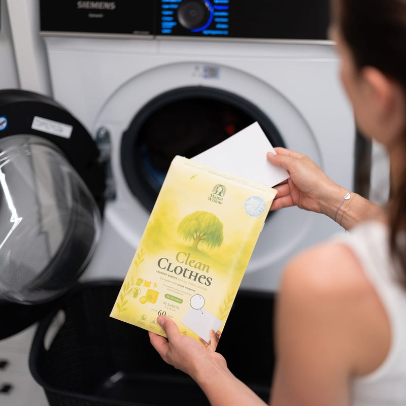 Hand legt ein Waschmittel-Blatt aus der Clean-Clothes-Packung in die Waschmaschine